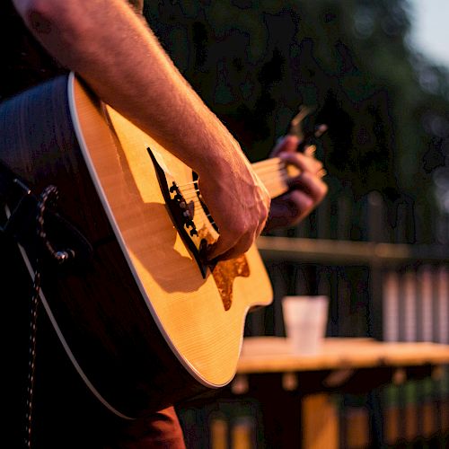 Person playing an acoustic guitar outside at dusk.